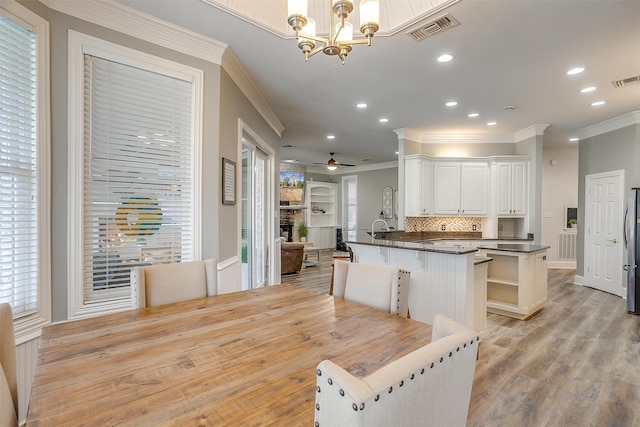 kitchen with light wood-type flooring, a kitchen bar, white cabinets, decorative light fixtures, and backsplash