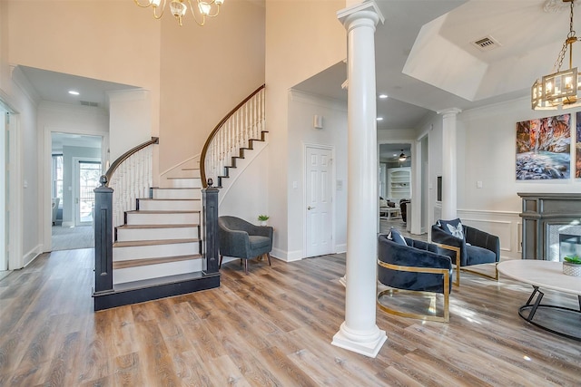 entryway with ornamental molding, wood-type flooring, decorative columns, and a notable chandelier