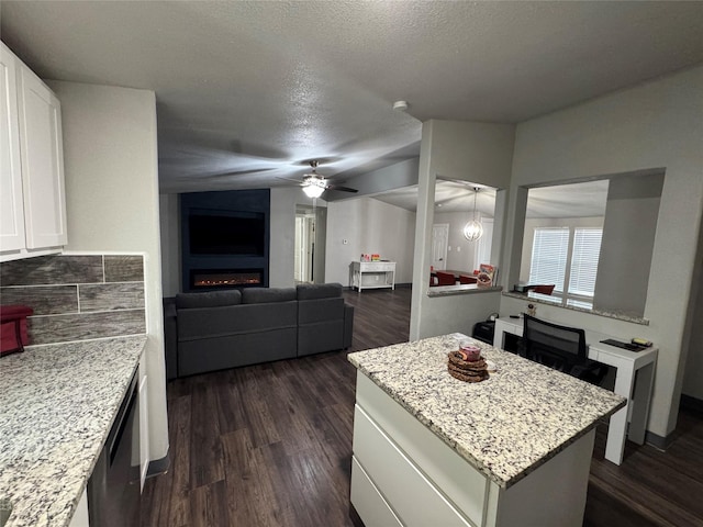 kitchen with light stone counters, a fireplace, a kitchen island, and white cabinetry