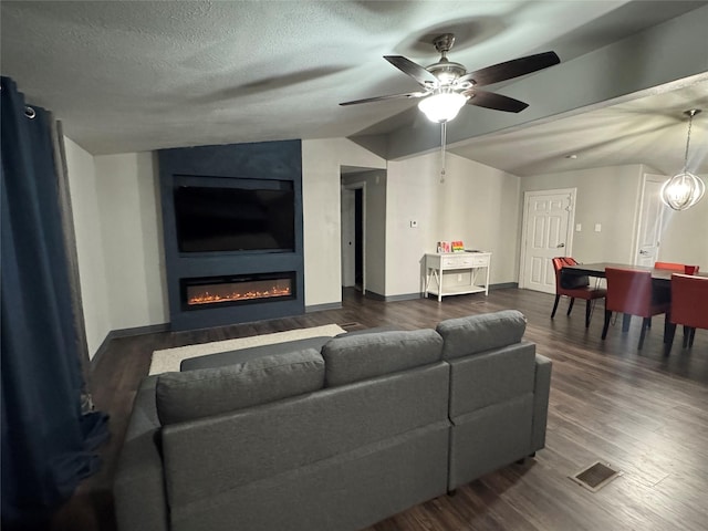 living area featuring baseboards, dark wood-style floors, vaulted ceiling, a textured ceiling, and ceiling fan with notable chandelier