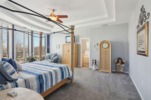 carpeted bedroom featuring ceiling fan, a tray ceiling, and ensuite bath