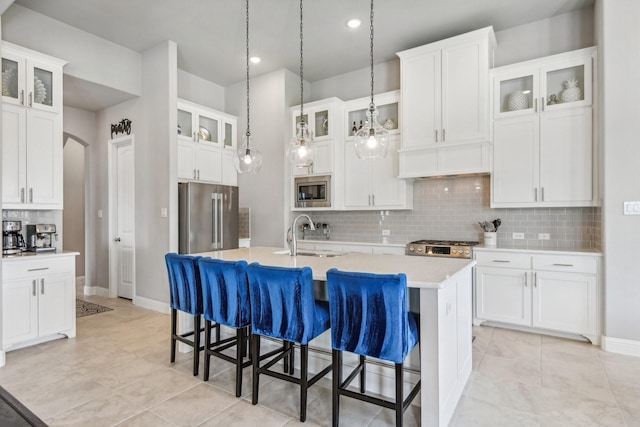 kitchen with appliances with stainless steel finishes, a kitchen island with sink, sink, white cabinets, and hanging light fixtures