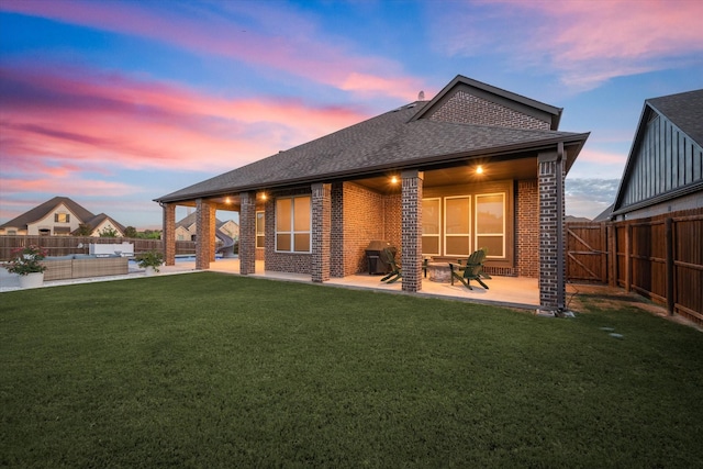 back house at dusk featuring an outdoor living space, a patio, and a lawn