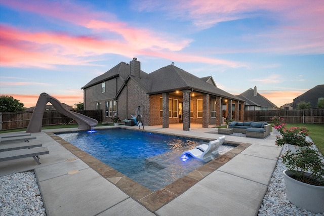 pool at dusk with an outdoor living space, a patio, and a water slide