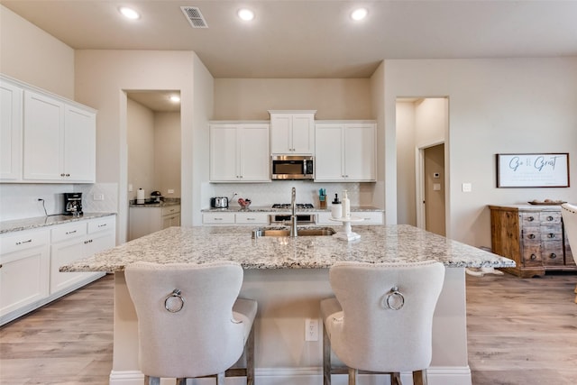 kitchen featuring light stone countertops, sink, a breakfast bar, and an island with sink