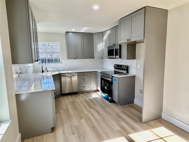 kitchen with gray cabinetry, sink, stainless steel appliances, tasteful backsplash, and light hardwood / wood-style floors