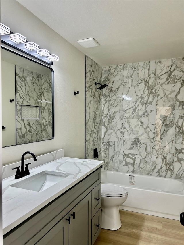 full bathroom featuring vanity, wood-type flooring, tiled shower / bath combo, and toilet