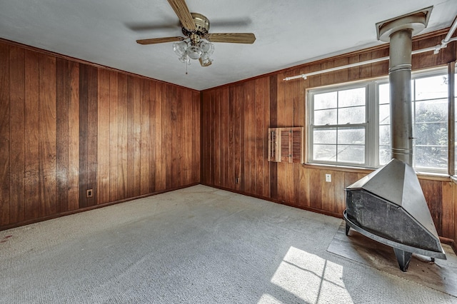 unfurnished room featuring ceiling fan, light colored carpet, a wood stove, and a wealth of natural light