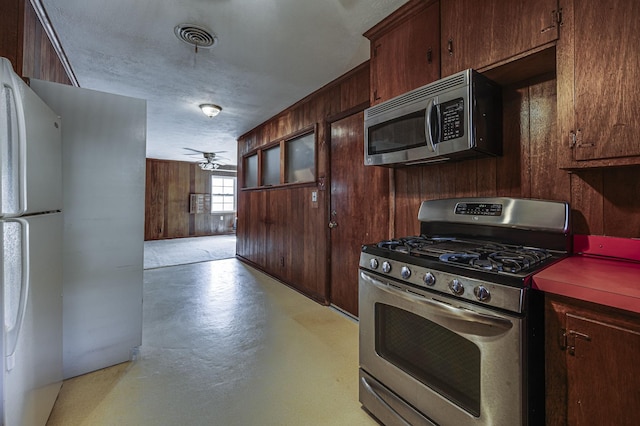 kitchen featuring ceiling fan, stainless steel appliances, wooden walls, and dark brown cabinetry