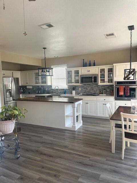 kitchen with dark hardwood / wood-style floors, white cabinets, decorative backsplash, hanging light fixtures, and stainless steel appliances