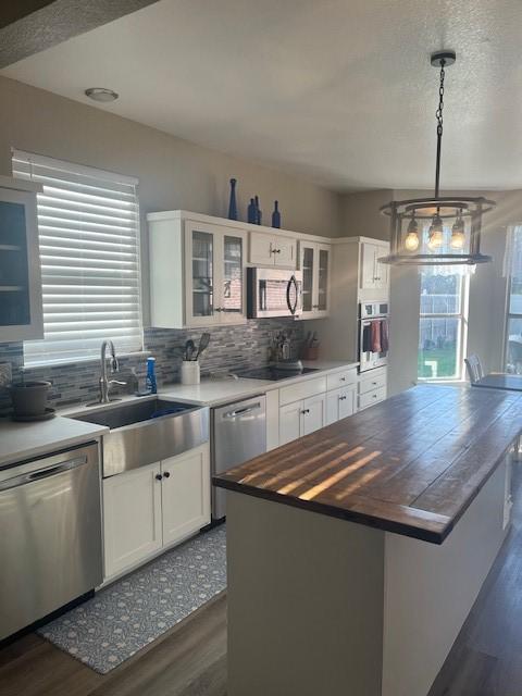 kitchen featuring white cabinetry, hanging light fixtures, wooden counters, a kitchen island, and appliances with stainless steel finishes