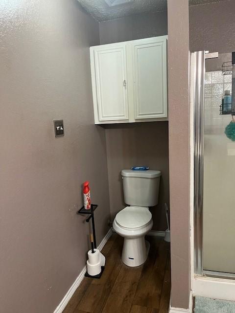 bathroom featuring toilet, an enclosed shower, a textured ceiling, and hardwood / wood-style flooring