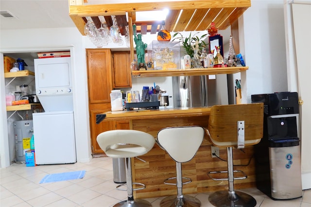 bar with stacked washer / drying machine, light tile patterned floors, and water heater