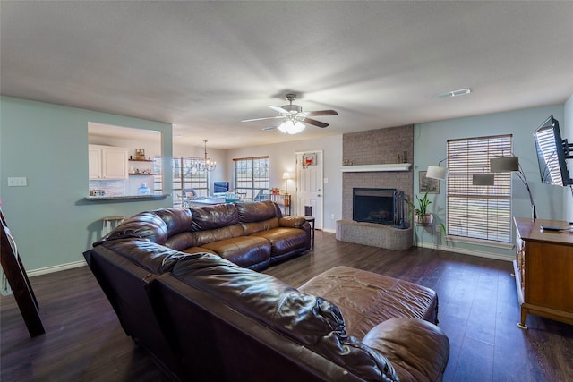 living room featuring ceiling fan with notable chandelier, a brick fireplace, and dark wood-type flooring