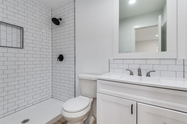 bathroom with decorative backsplash, toilet, a tile shower, and vanity