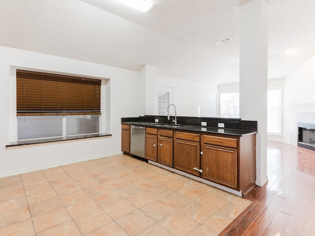 kitchen with a tiled fireplace, dishwasher, a textured ceiling, and sink