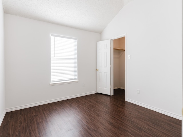 unfurnished bedroom featuring dark hardwood / wood-style flooring, a textured ceiling, vaulted ceiling, a spacious closet, and a closet