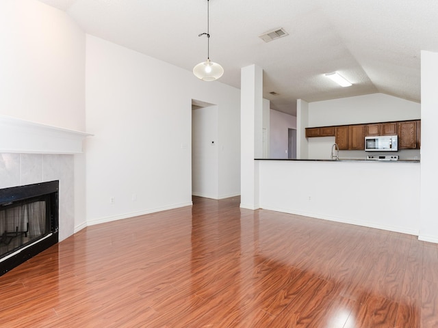 unfurnished living room featuring hardwood / wood-style flooring, lofted ceiling, and a tiled fireplace