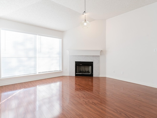 unfurnished living room featuring a textured ceiling, hardwood / wood-style flooring, vaulted ceiling, and a tiled fireplace