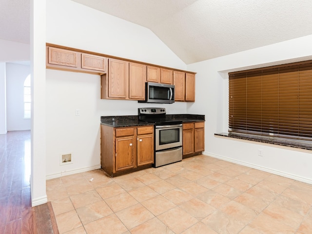 kitchen featuring dark stone countertops, light tile patterned floors, stainless steel appliances, and lofted ceiling