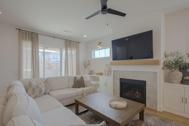 living room featuring a tiled fireplace, light hardwood / wood-style flooring, and ceiling fan