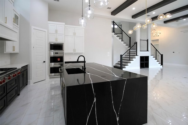 kitchen with white cabinets, a center island with sink, sink, appliances with stainless steel finishes, and beamed ceiling