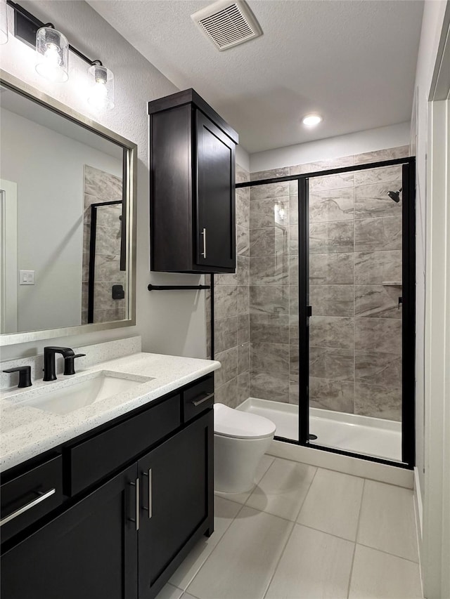 bathroom featuring vanity, a shower with door, tile patterned flooring, toilet, and a textured ceiling