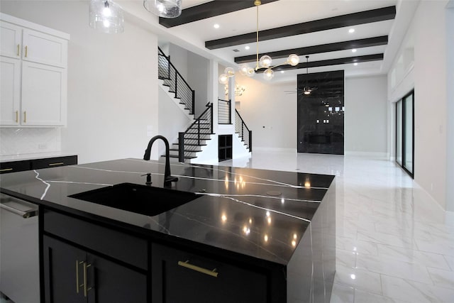 kitchen featuring beam ceiling, sink, hanging light fixtures, a center island with sink, and white cabinets