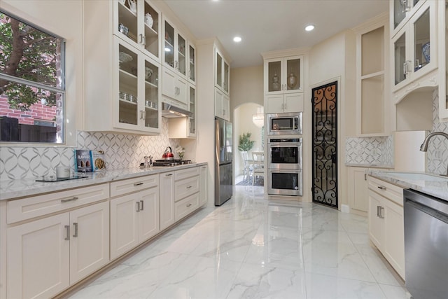 kitchen with arched walkways, stainless steel appliances, a sink, marble finish floor, and light stone countertops