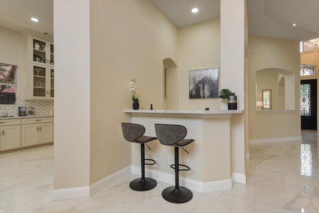 kitchen with baseboards, arched walkways, glass insert cabinets, a breakfast bar area, and marble finish floor