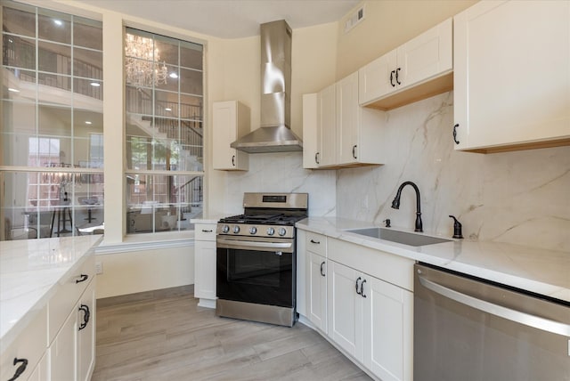 kitchen with a sink, appliances with stainless steel finishes, wall chimney range hood, and light stone countertops