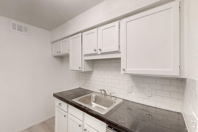 kitchen with white cabinets, backsplash, light hardwood / wood-style floors, and sink