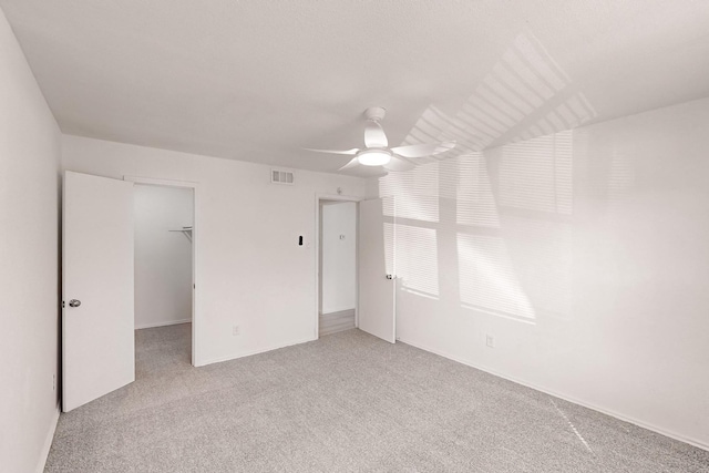 unfurnished bedroom featuring a closet, a spacious closet, ceiling fan, and light colored carpet