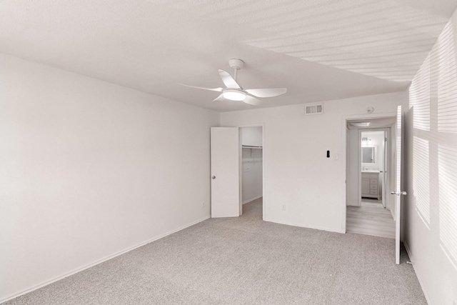 unfurnished bedroom with a walk in closet, ceiling fan, a closet, and light carpet