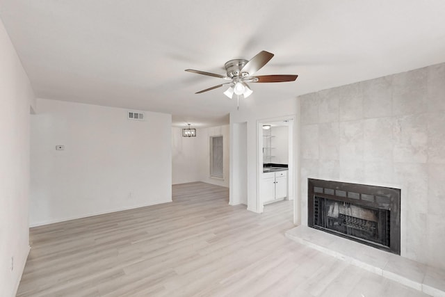 unfurnished living room featuring ceiling fan, a large fireplace, and light hardwood / wood-style floors