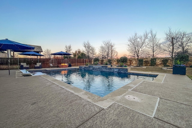 pool at dusk with pool water feature and a patio area