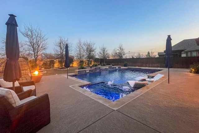 pool at dusk with pool water feature, a patio area, and a jacuzzi