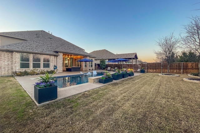 pool at dusk with a patio and a lawn