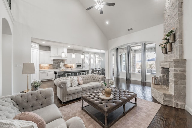 living room featuring hardwood / wood-style floors, high vaulted ceiling, ceiling fan, and a stone fireplace