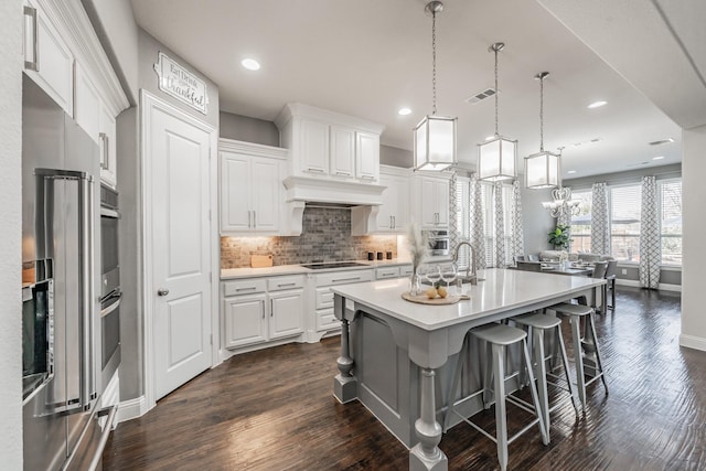 kitchen with white cabinets, a kitchen island with sink, pendant lighting, and dark hardwood / wood-style floors