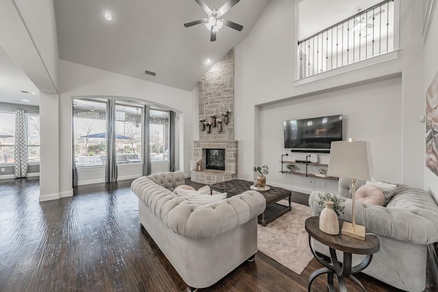 living room featuring high vaulted ceiling, ceiling fan, dark hardwood / wood-style flooring, and a stone fireplace