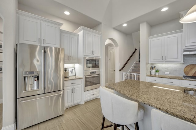 kitchen with white cabinetry, appliances with stainless steel finishes, light stone counters, and decorative backsplash