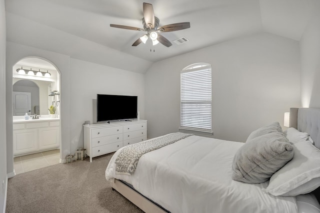 bedroom featuring ceiling fan, light colored carpet, lofted ceiling, and ensuite bath