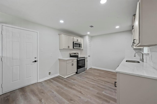 kitchen with light stone countertops, decorative backsplash, stainless steel appliances, sink, and white cabinets