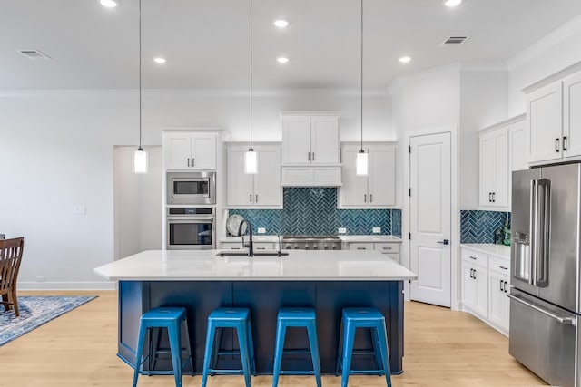 kitchen with appliances with stainless steel finishes, decorative light fixtures, a kitchen island with sink, and sink