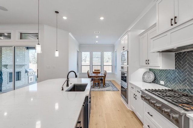 kitchen featuring light stone countertops, sink, stainless steel appliances, decorative light fixtures, and white cabinets