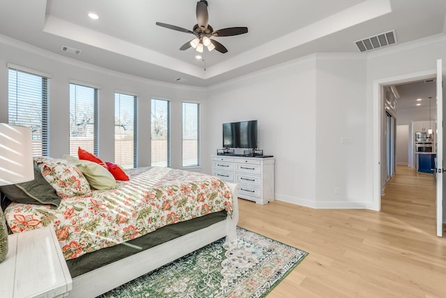 bedroom featuring light hardwood / wood-style flooring, a raised ceiling, ceiling fan, and ornamental molding