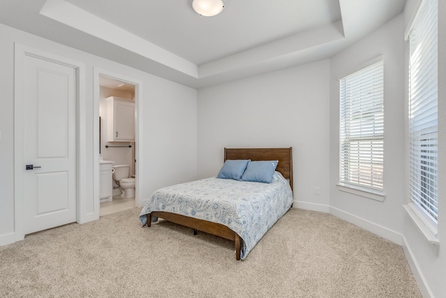 carpeted bedroom with a tray ceiling and ensuite bathroom