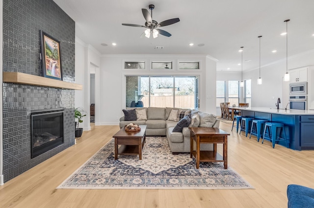 living room with a tiled fireplace, ceiling fan, crown molding, and light hardwood / wood-style floors