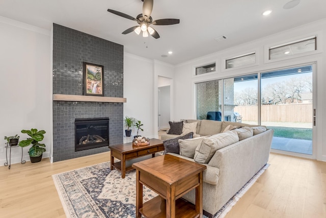 living room with a tiled fireplace, ceiling fan, light hardwood / wood-style flooring, and ornamental molding